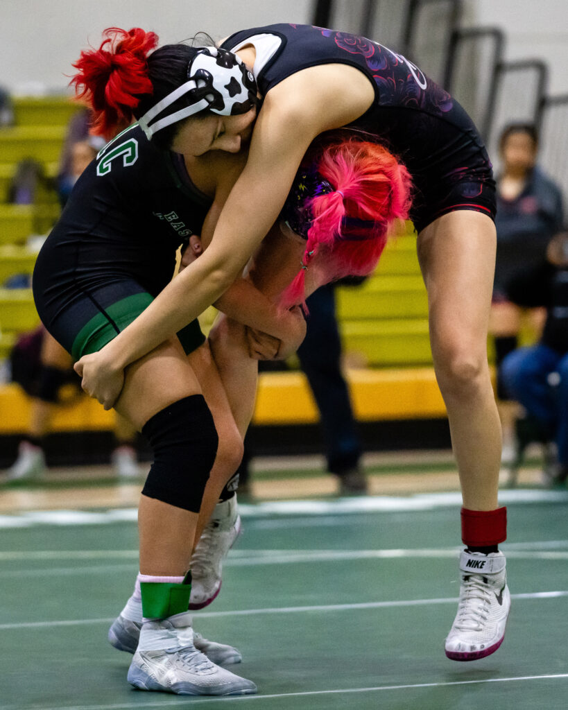 Mollie Jimenez vs Stephany Zamora, 109-pound weight class. Jimenez with pink hair and Zamora with red hair. Here Zamora is wrapped over Jimenez' back as Jimenez tries to lift her off the mat. 