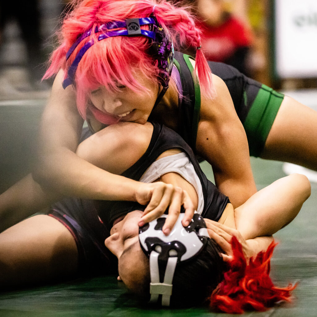 Close-up image of one wrestler on top of another attempting to pin her.