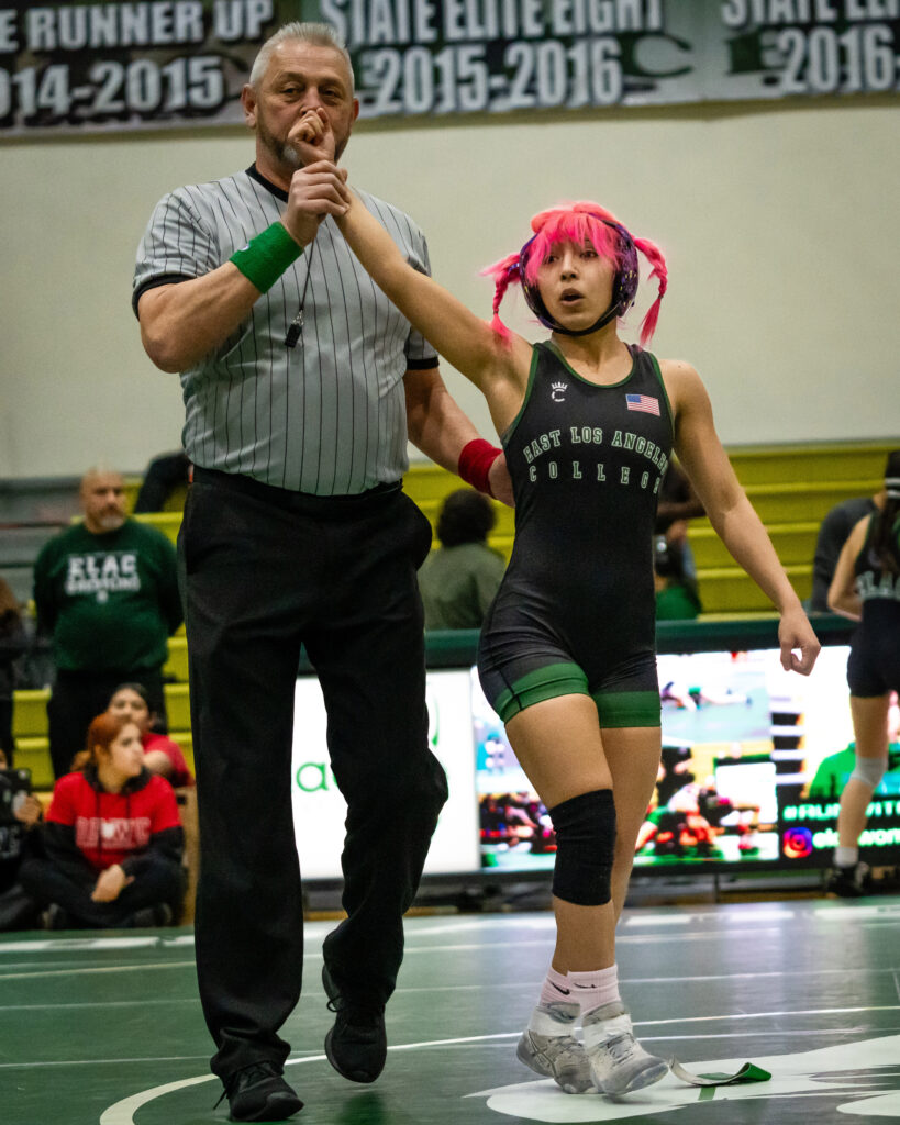Leader of the Pack wrestling tournament at East Los Angeles College. A referee holds up Mollie Jimenez' hand indicating that she has won the bout in the 109-pound weight class. 